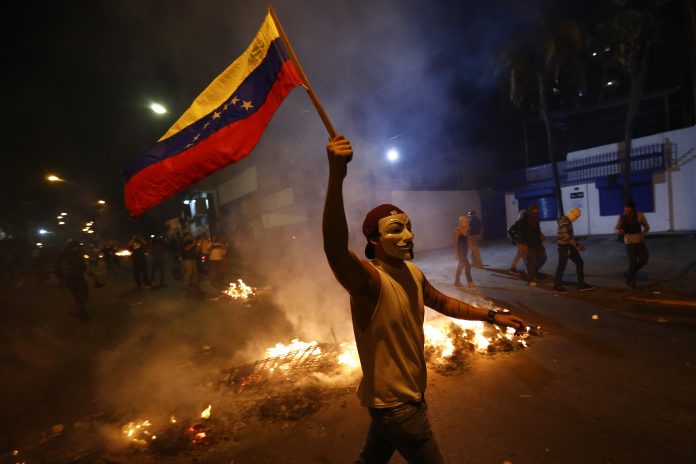 An opposition demonstrators holds a Venezuelan flag in front of a burning barricade in Caracas
